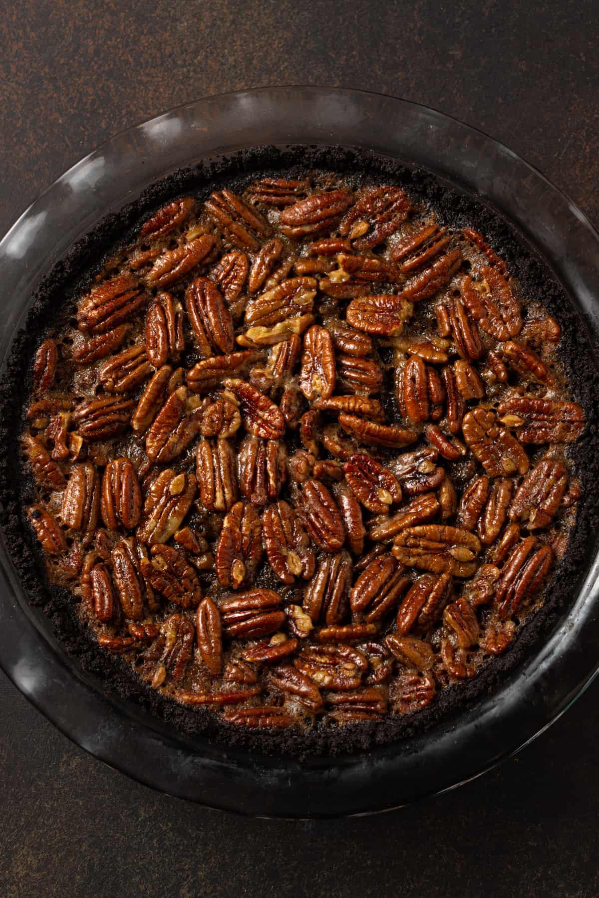 Whole pecan pie in a glass pie plate on a brown background.