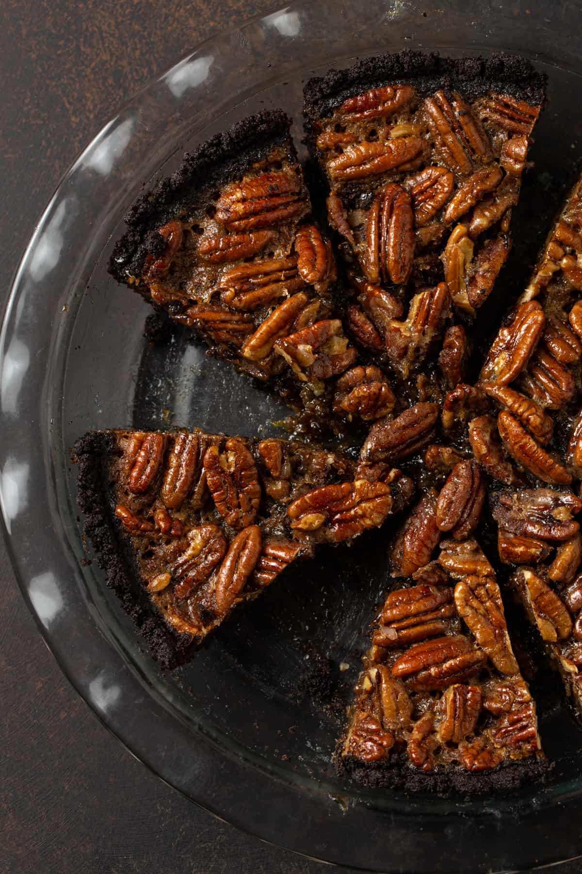 Slices of pecan pie cut in a glass pie plate on a brown background. 