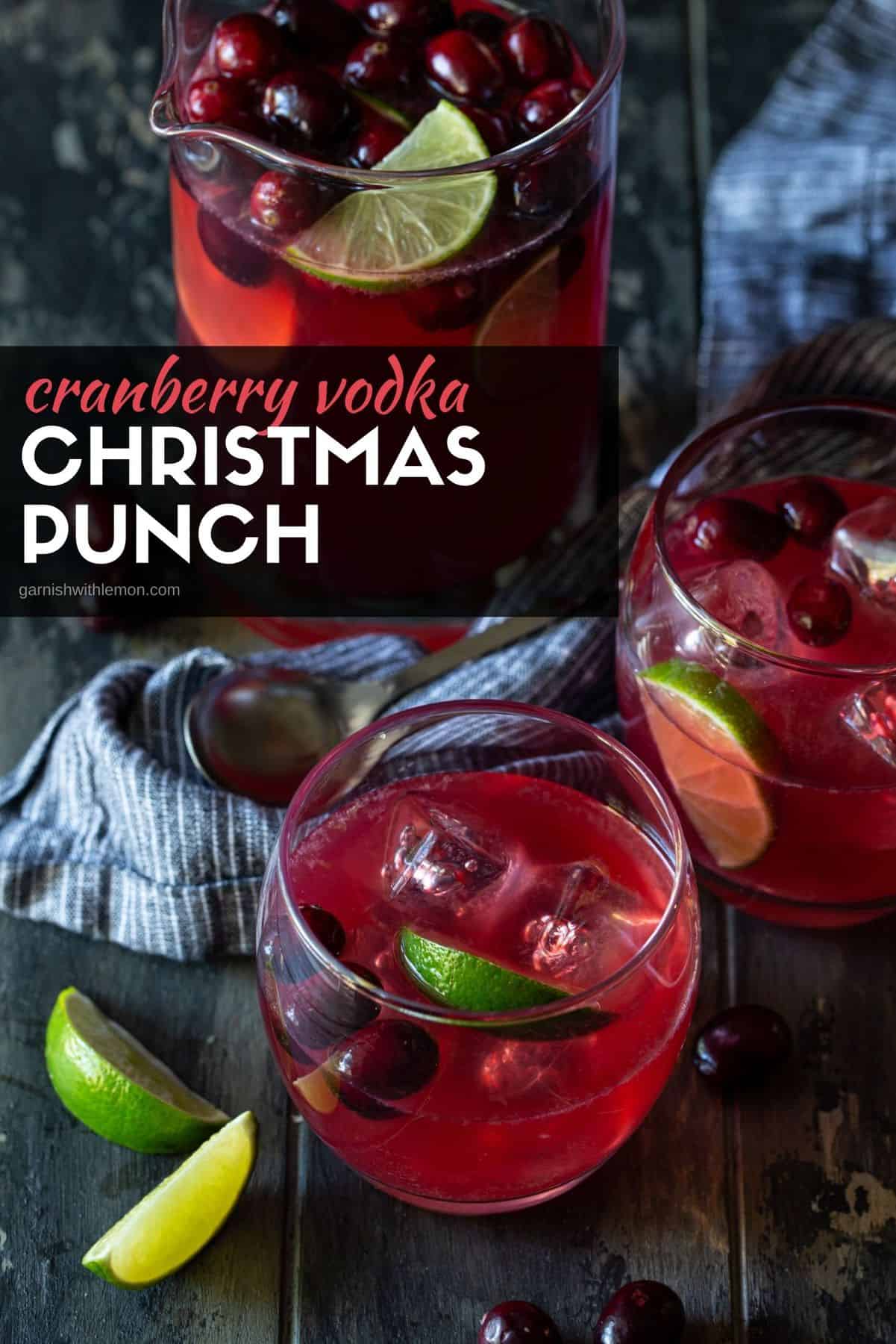 Two glasses of punch garrnished with fresh cranberries and lime wedges with a pitcher of punch in the background. 