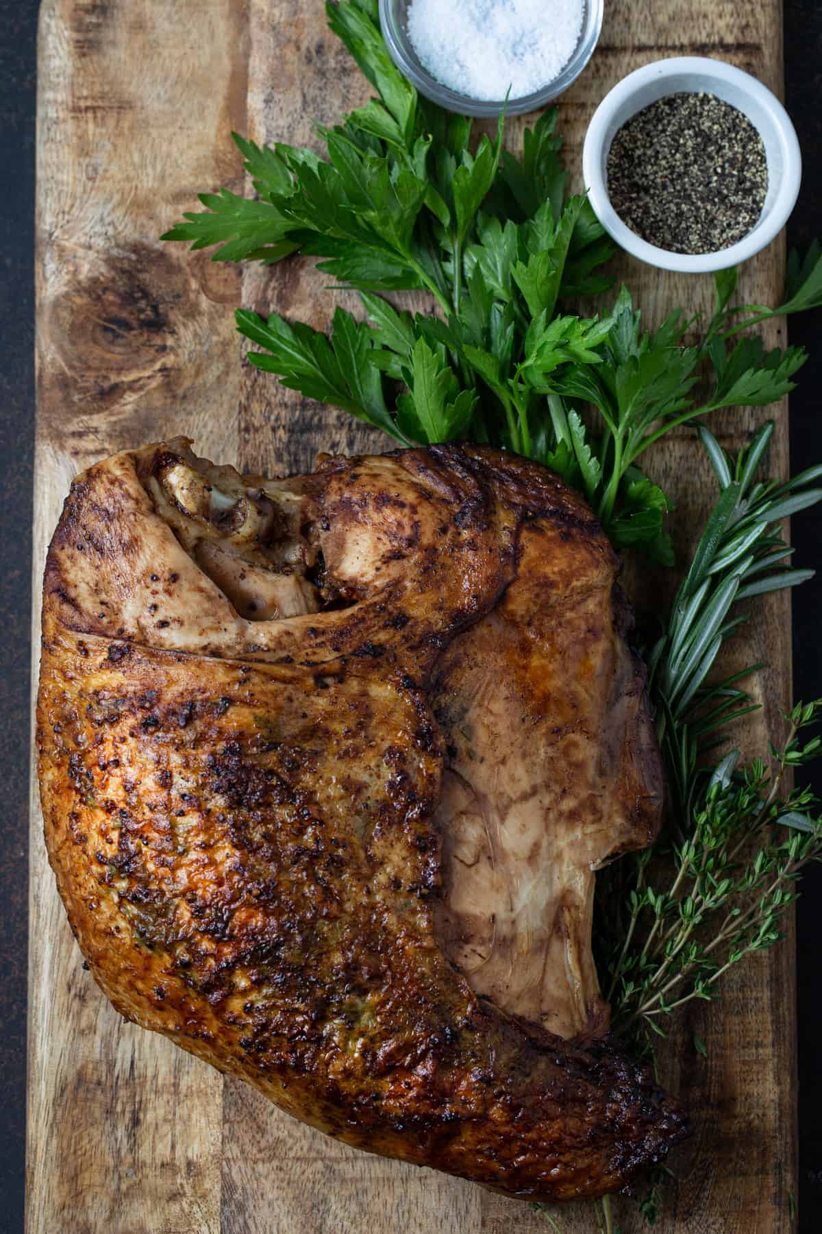 Roasted skin on turkey breast on cutting board with fresh herbs.