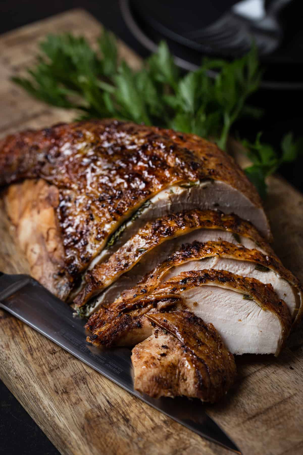 Aliced roasted turkey breast on a cutting board with a knife.