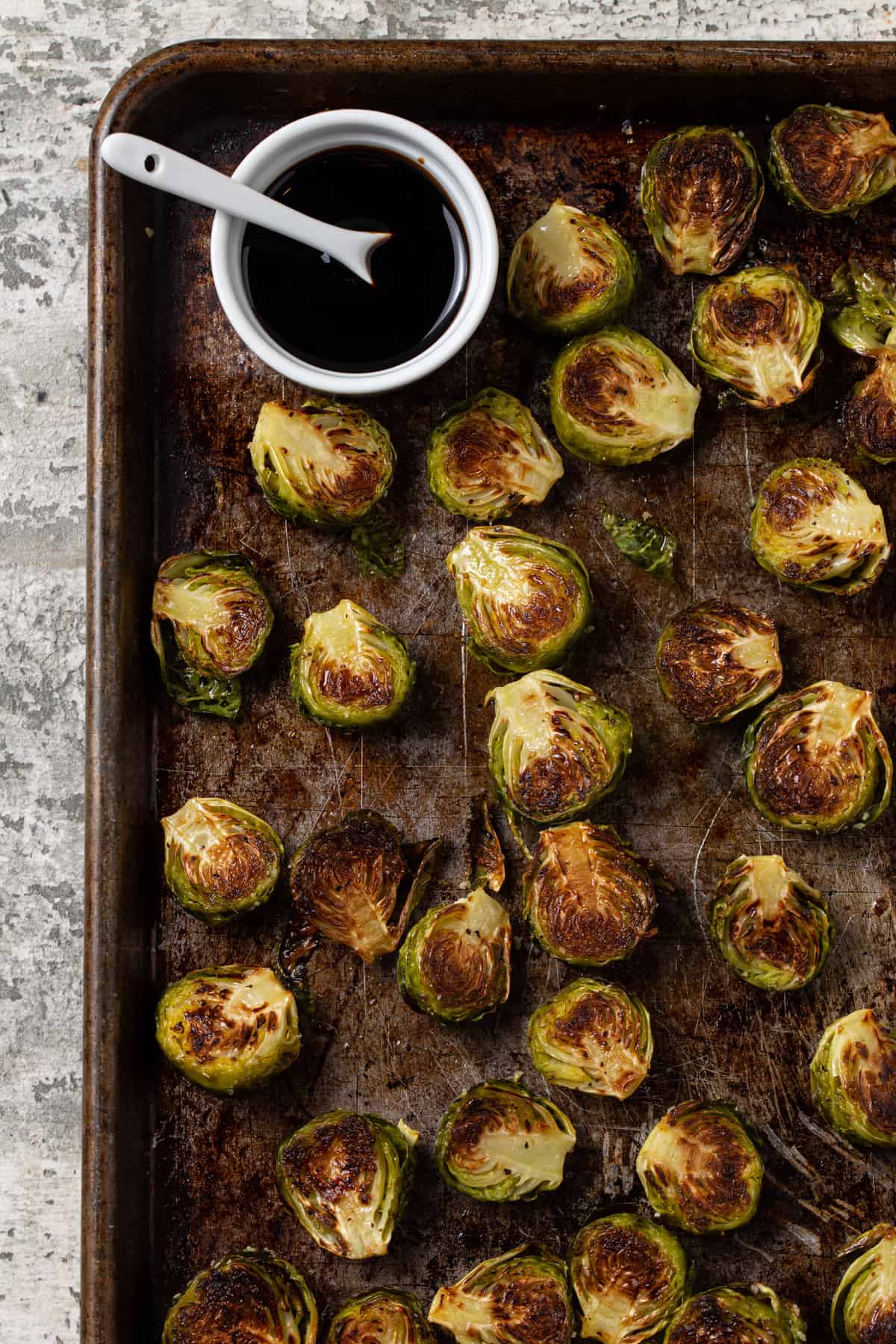 Large sheet pan with roasted brussels sprouts with small white bowl filled with balsamic reduction