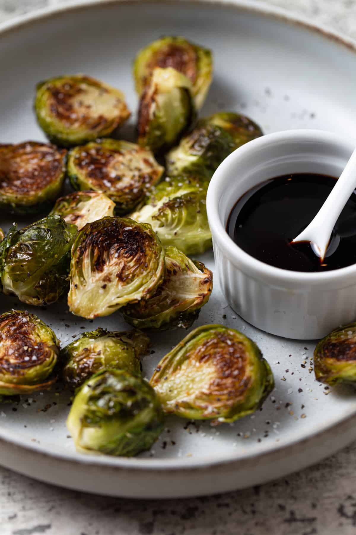 brussels sprouts cut in half on plate that have been cooked with balsamic reduction on side