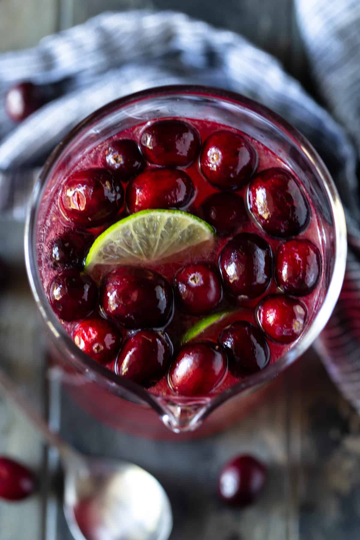 Cranberries and lime wedges floating on the top of punch in a pitcher.