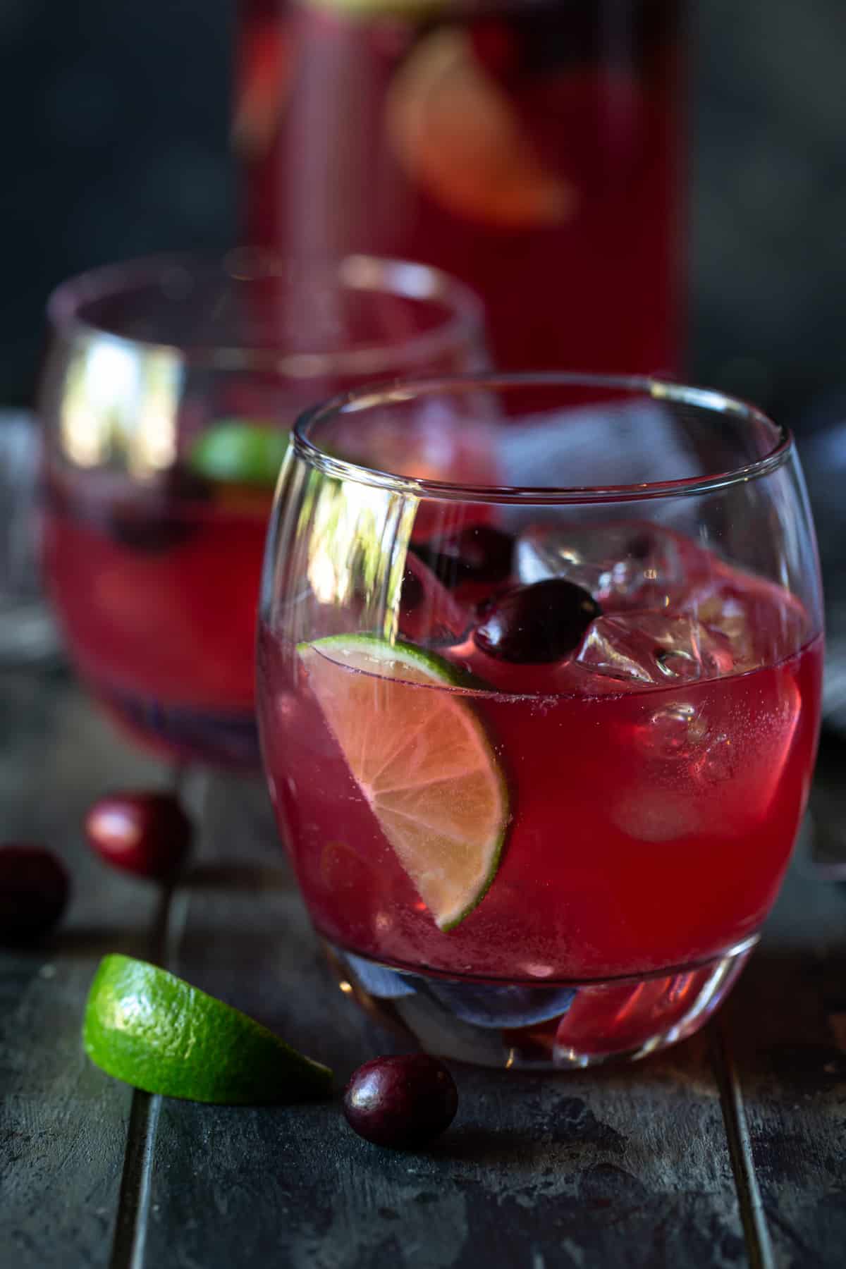 two glasses of punch in ice-filled glasses with lime wedges and fresh cranberries