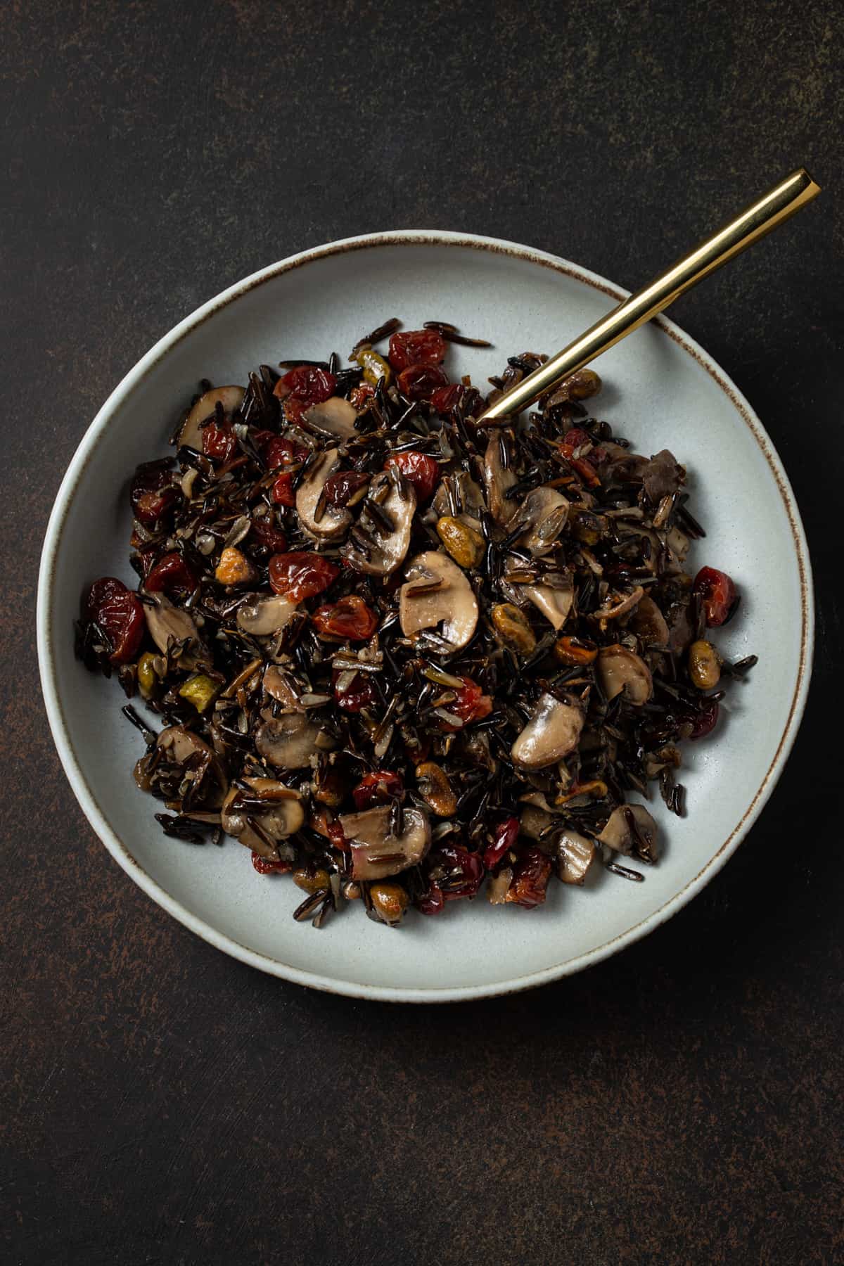 Gray bowl filled with cooked wild rice, mushrooms, cherries & pistachios. 