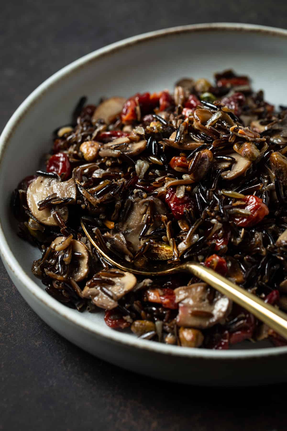 gray bowl filled with cooked wild rice, cherries, mushrooms & pistachios. 