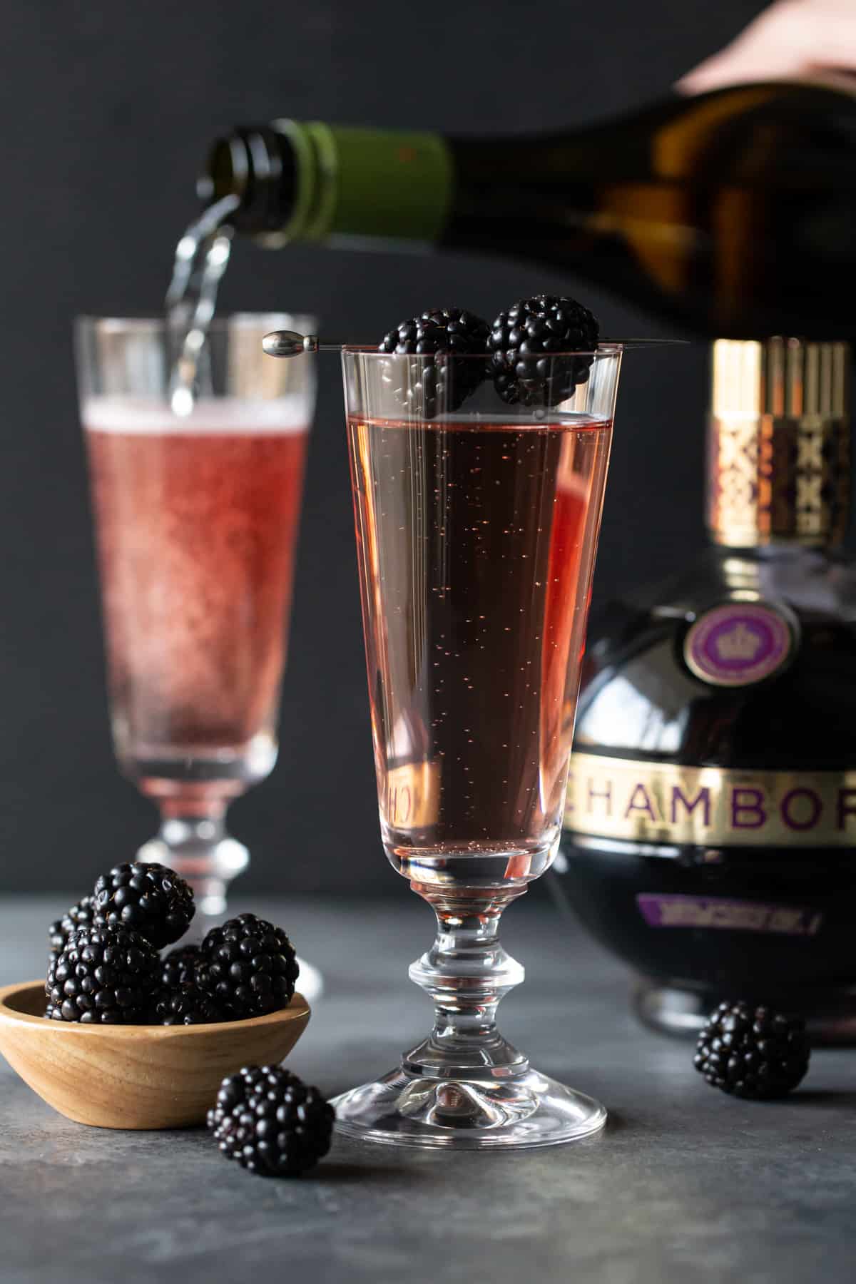 Flutes of cocktail on a dark board with blackberries. 