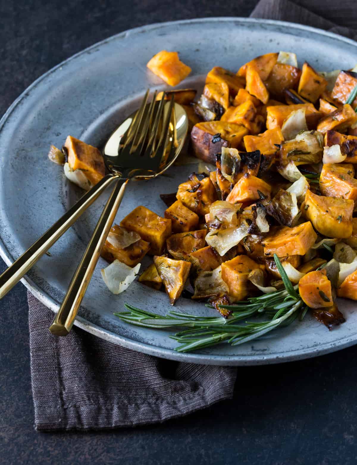 Roasted potatoes & onions on a silver plate with flatware. 