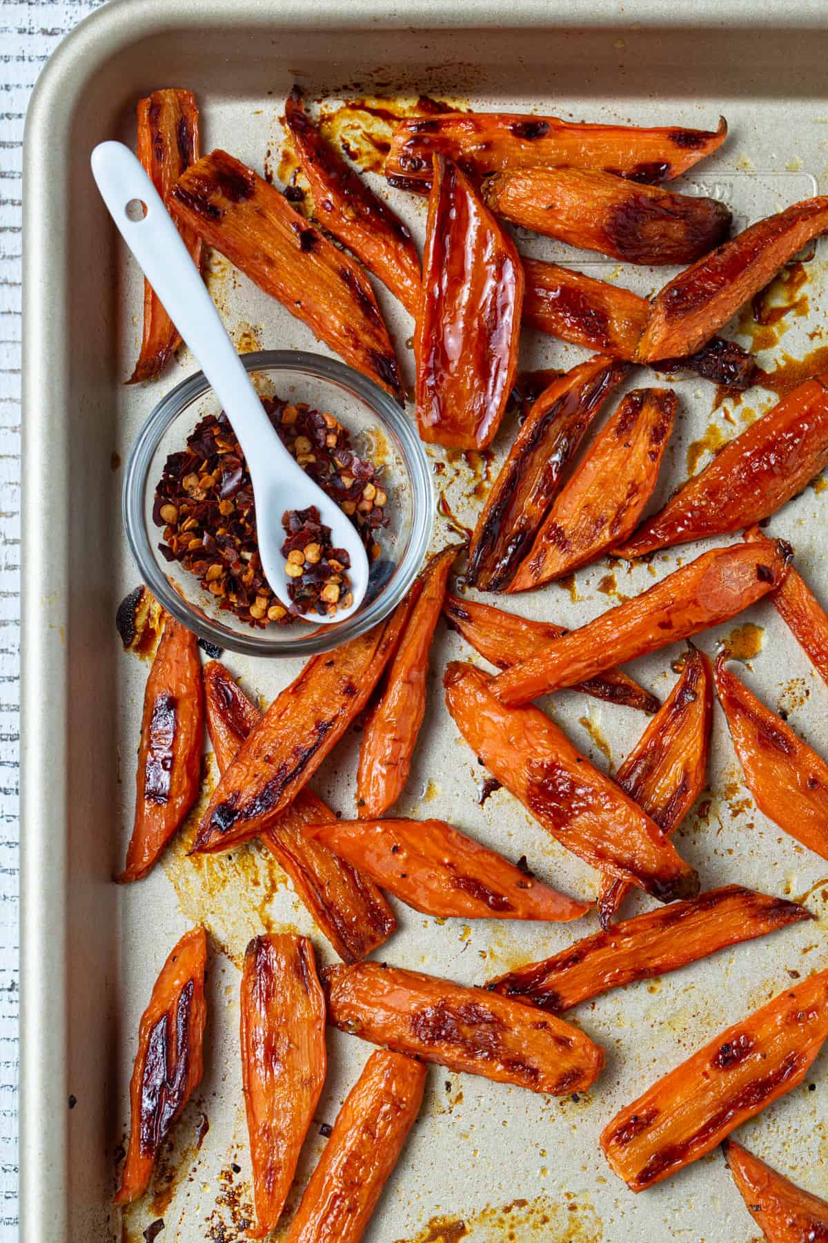 Roasted carrots on a sheet pan with bowl of crushed red pepper. 