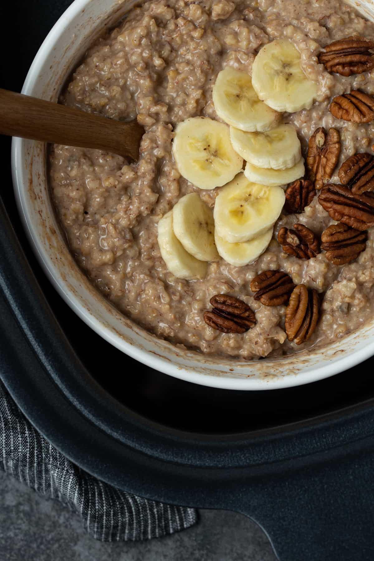 A large bowl of oatmeal in a slow cooker with bananas and pecans.