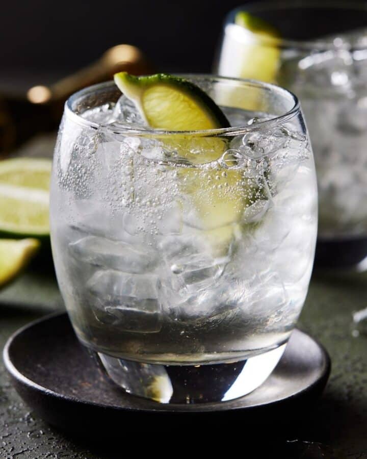 Gin and tonic cocktail in lowball glass with ice and lime wedge.