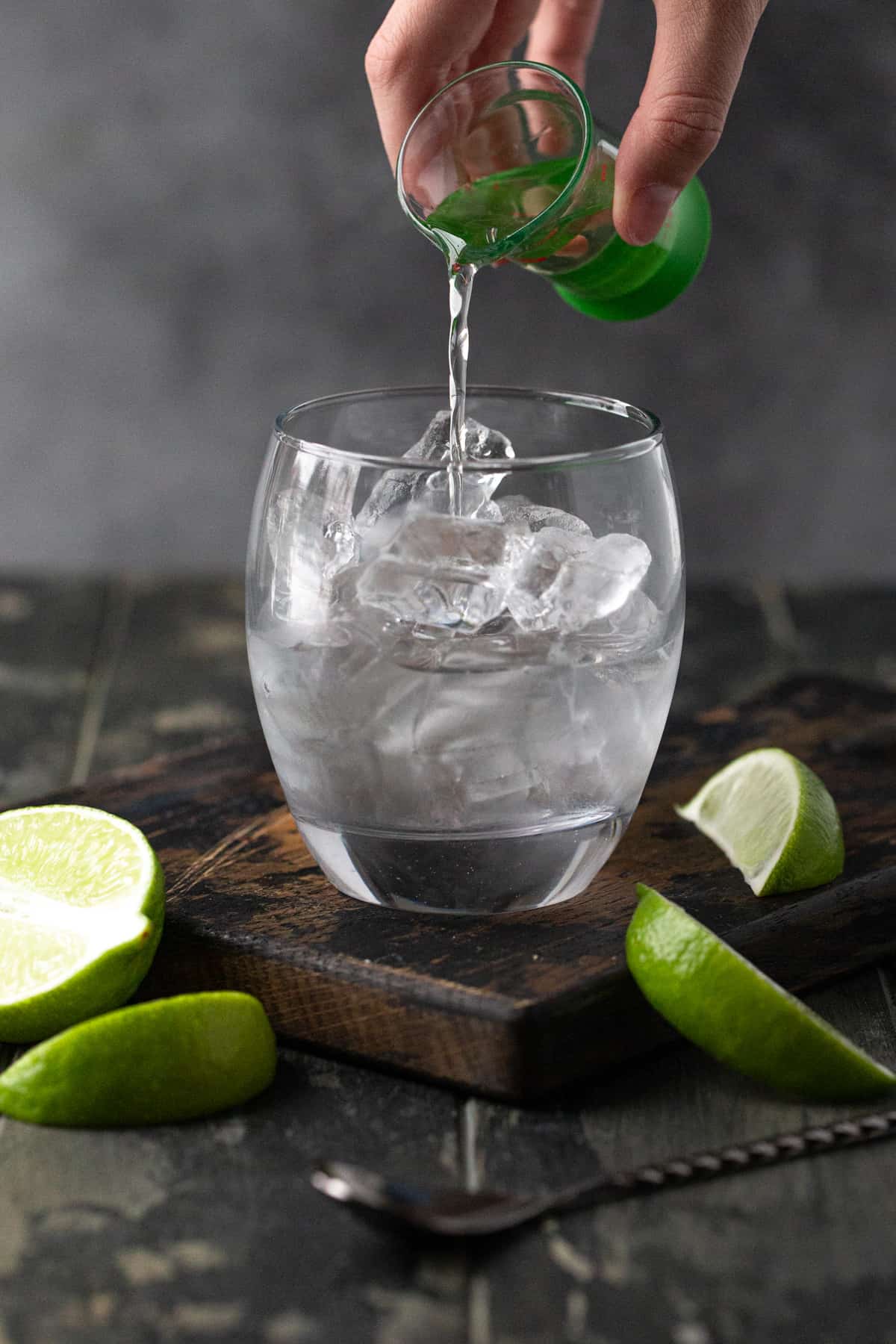 Hand pouring gin into a lowball glass filled with ice.