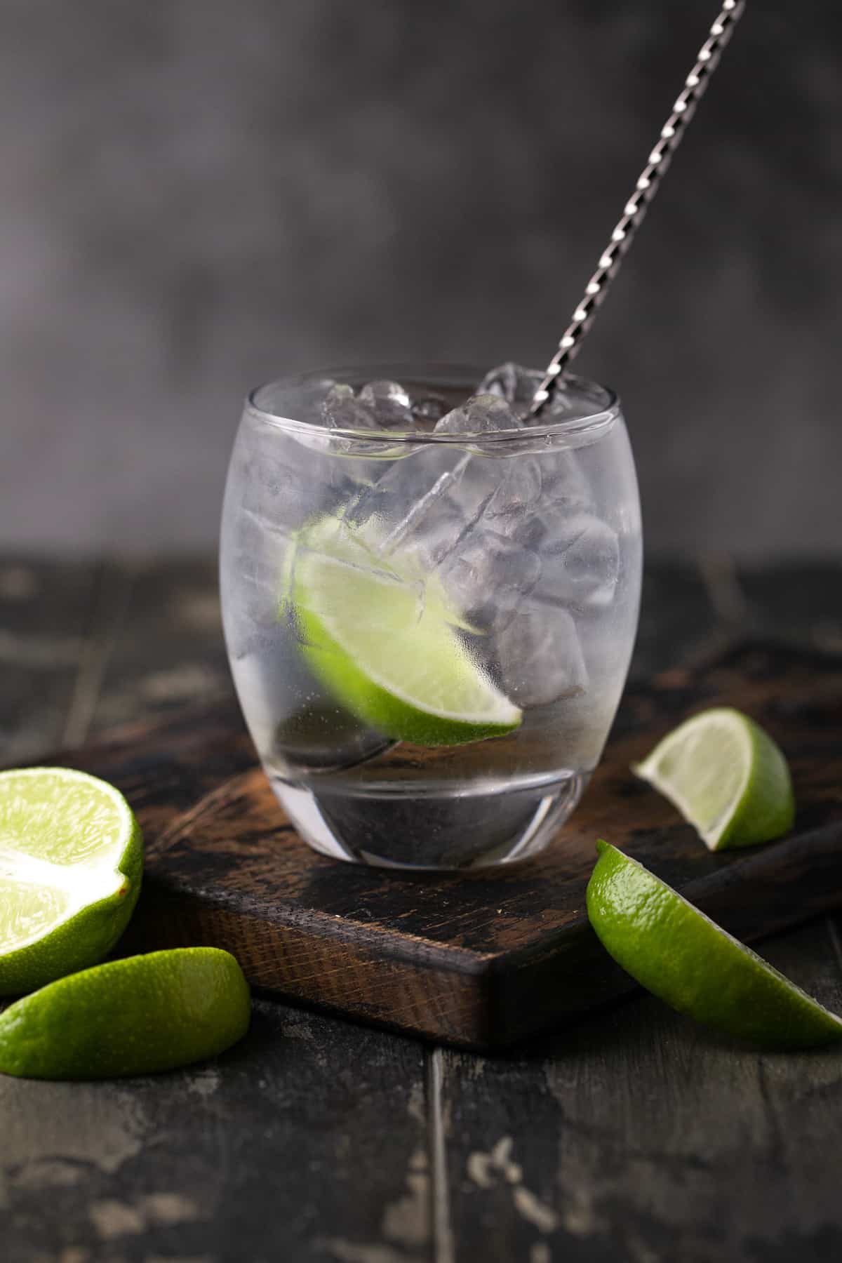 Bar spoon in a lowball glass filled with ice, elderflower gin and tonic and a lime wedge.