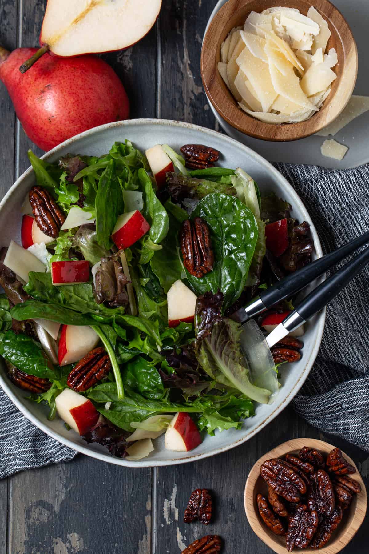 Pear salad in a gray bowl surrounded by pecans and parmesan cheese.