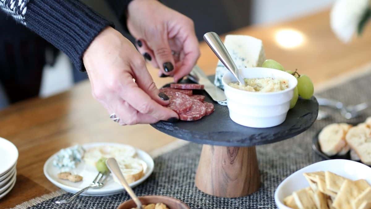 Hands arranging charcuterie on a round slate board. 