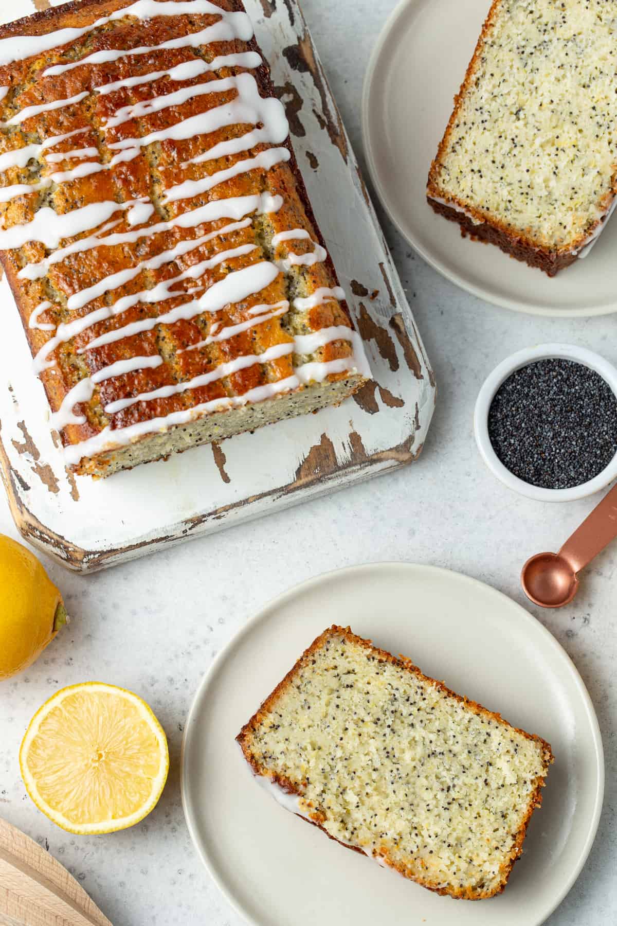 Slices of lemon poppy seed bread on white plates. Loaf on lemon poppy seed bread on a white wooden cutting board.