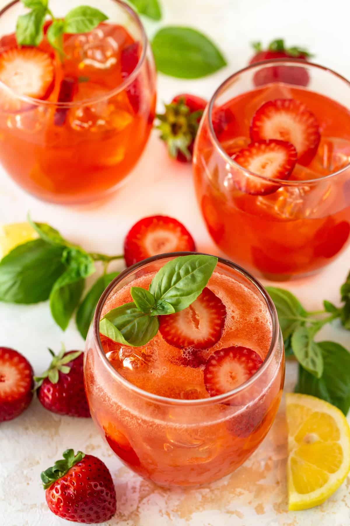 Pink cocktails in lowball glasses filled with ice and garnished with strawberries and basil. 
