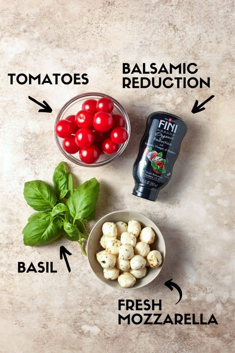 Ingredients for Caprese Skewers including cherry tomatoes, fresh mozzella balls, basil and balsamic glaze. 