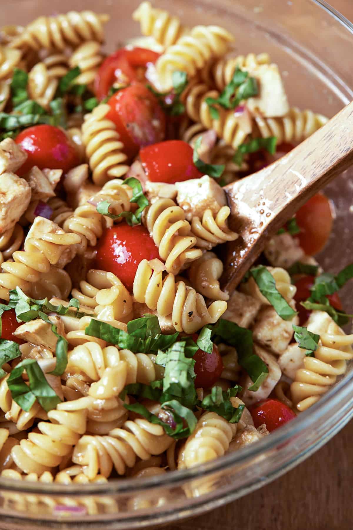 Glass bowl with pasta, basil, tomatoes and spoon.