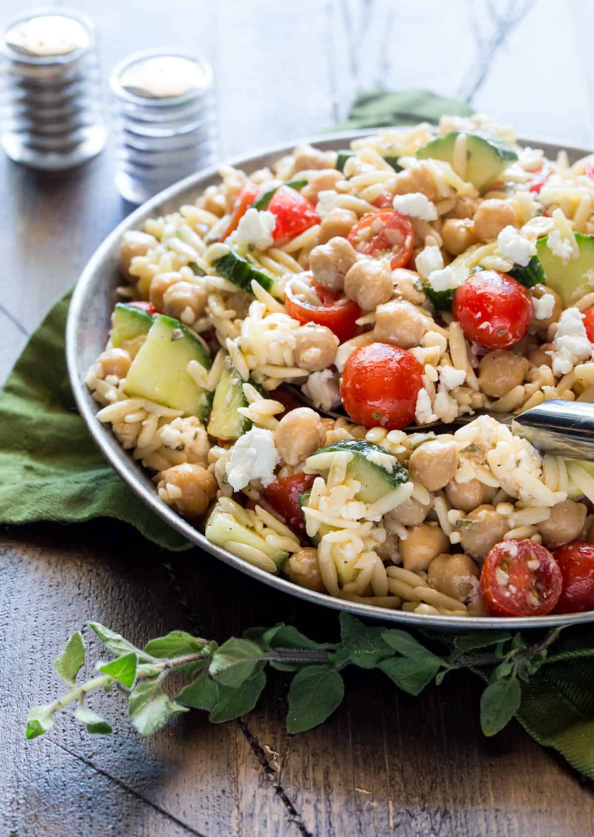 Chickpea Salad recipe in a silver dish on a wood board. Garnished with fresh oregano. 