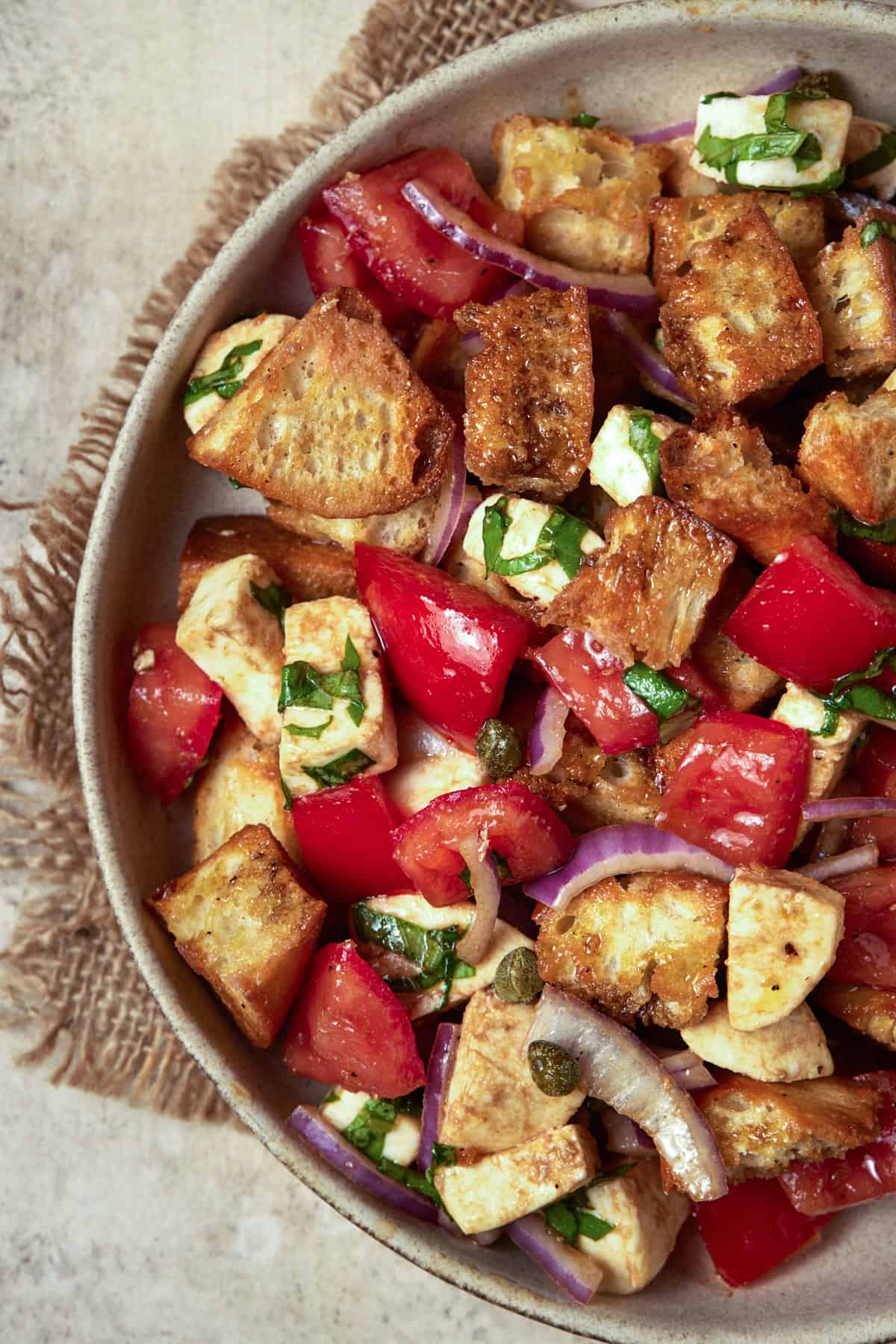 Bread and tomato salad in a ceramic bowl on a burlap napkin.