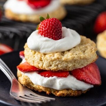 Strawberry shortcake biscuit on a black plate with a fork on the side.