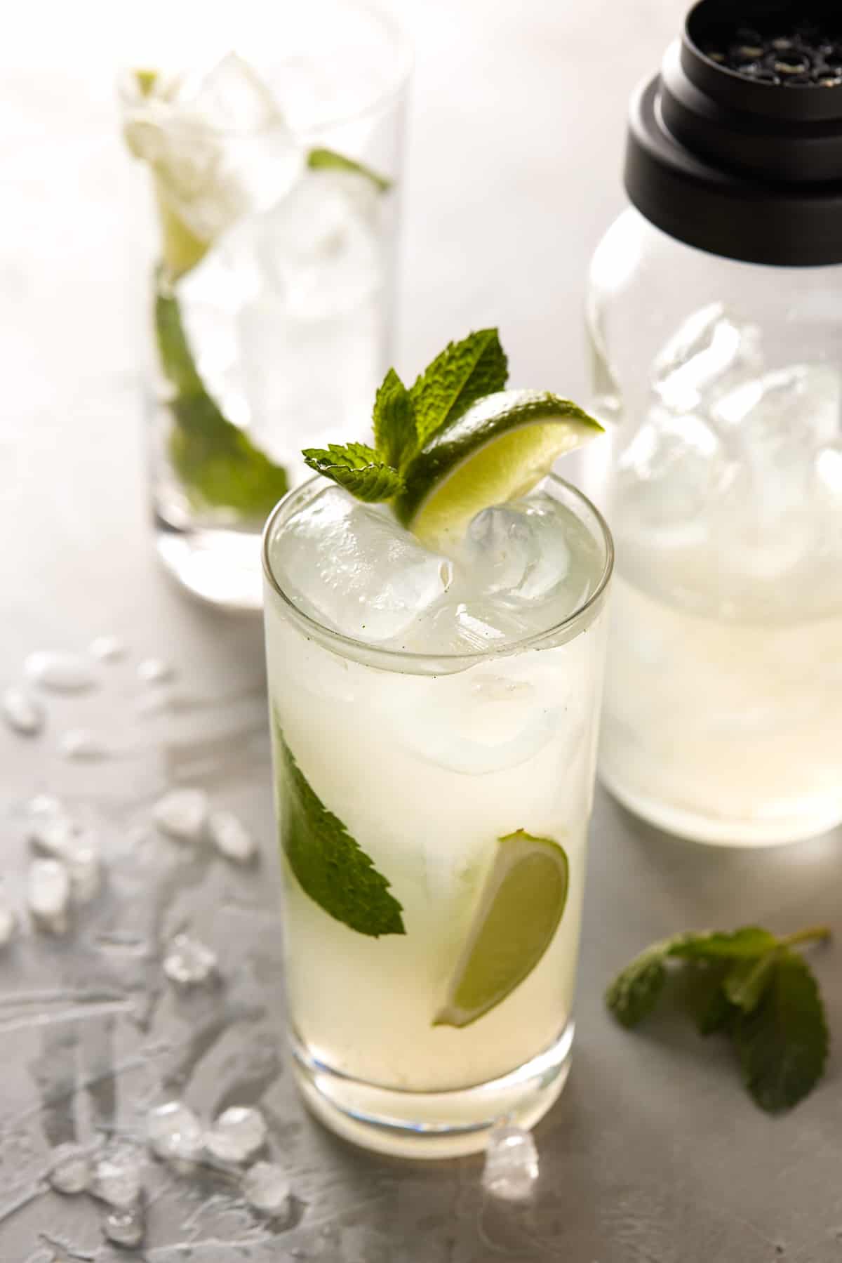 High ball glass filled with drink and garnished with mint leaves and lime wedges.