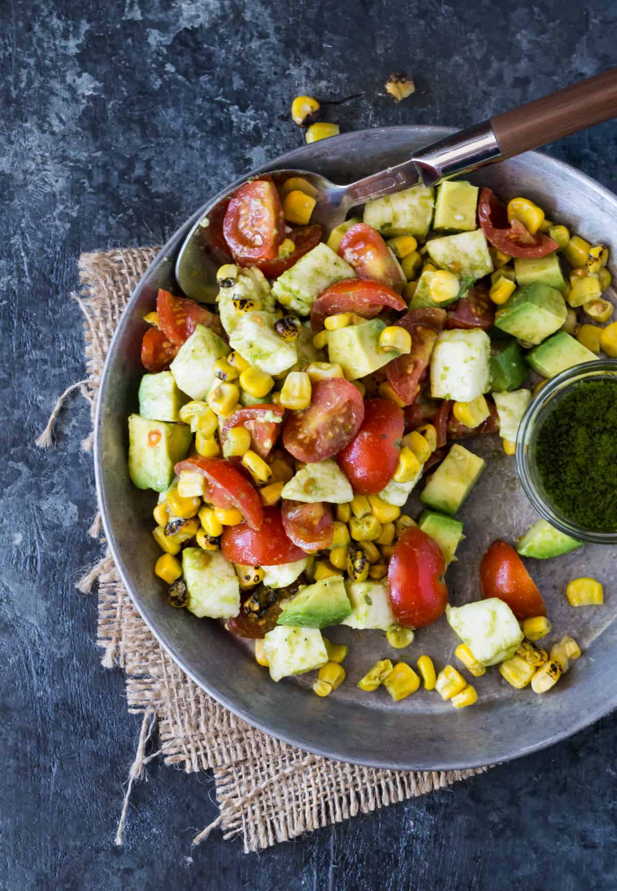 Silver bowl of Tomato, Mozzarella and Grilled Corn Salad on a burlap napkin.