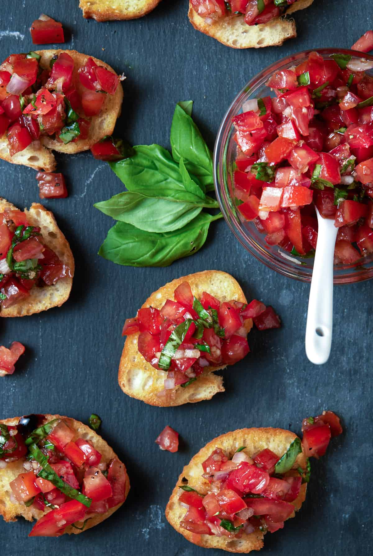 crostini on slate board with chopped tomatoes and herbs on top.