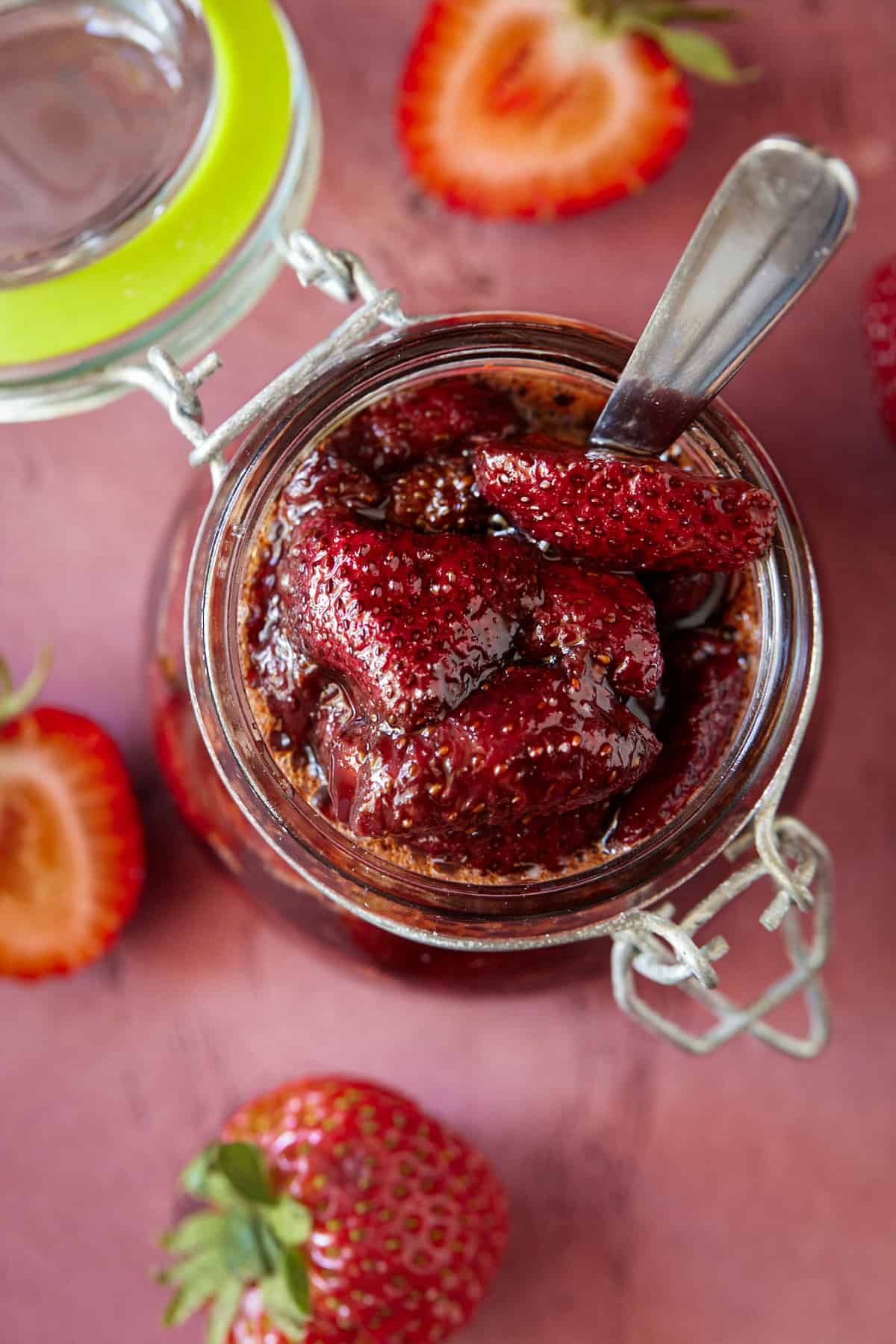 Glass jar of strawberry sauce with a spoon. 