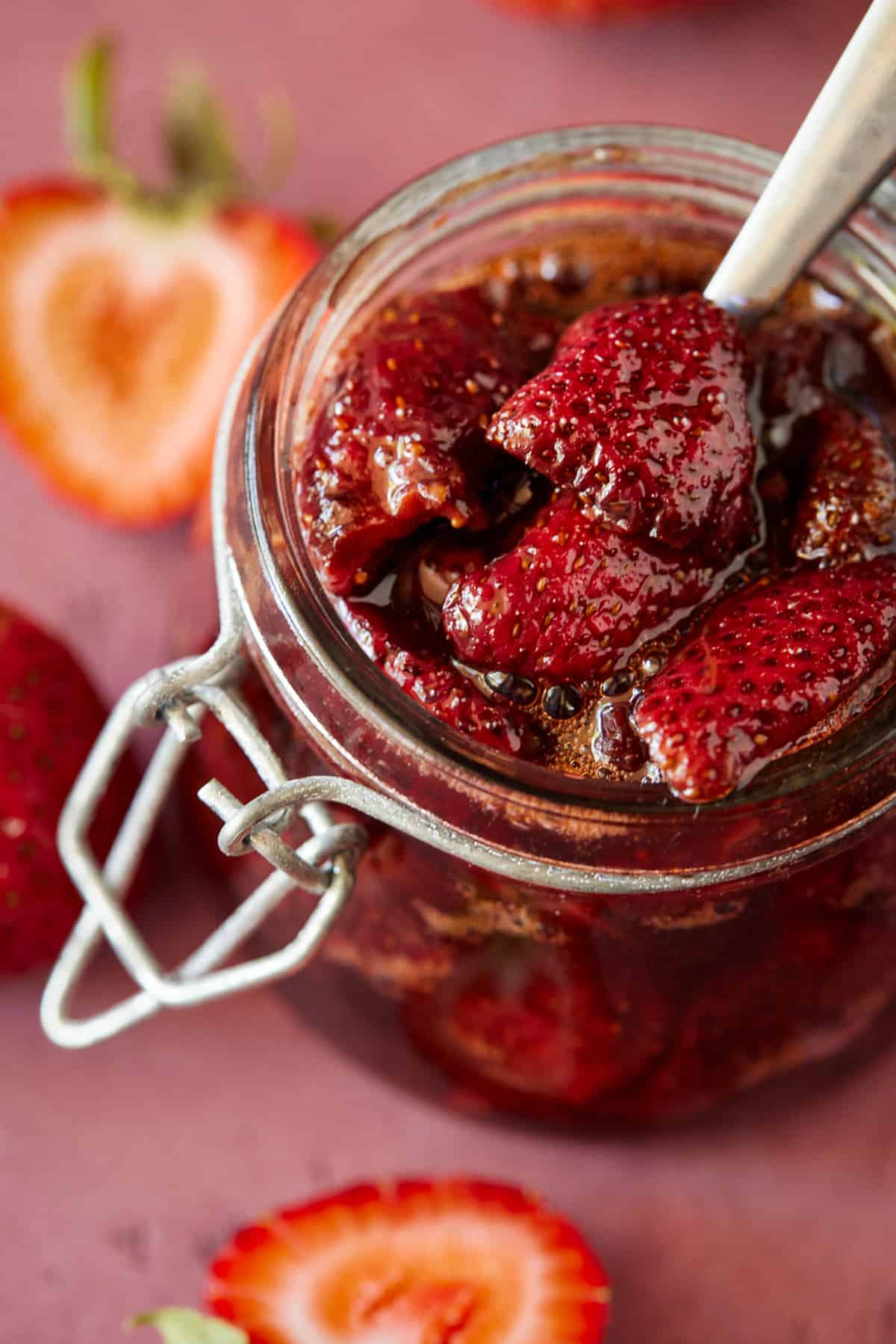 Spoon in glass jar of strawberry sauce. 
