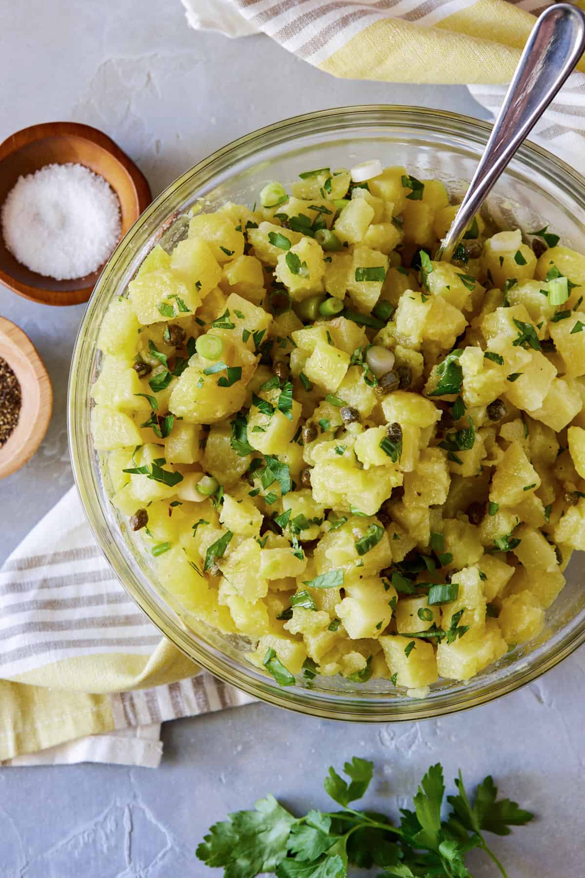 glass bowl filled with cooked potatoes, parsley and capers. 