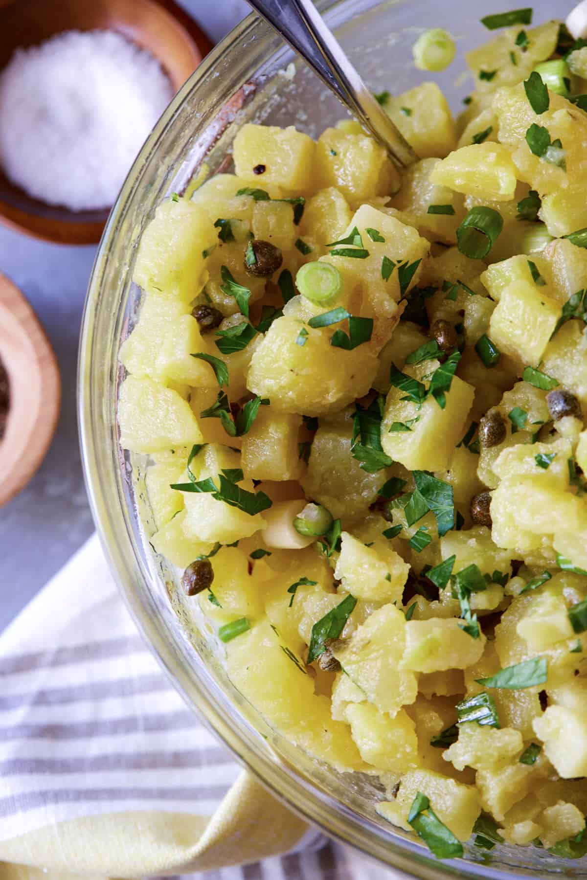 Glass bowl filled with diced potatoes, parley, green onions and capers.