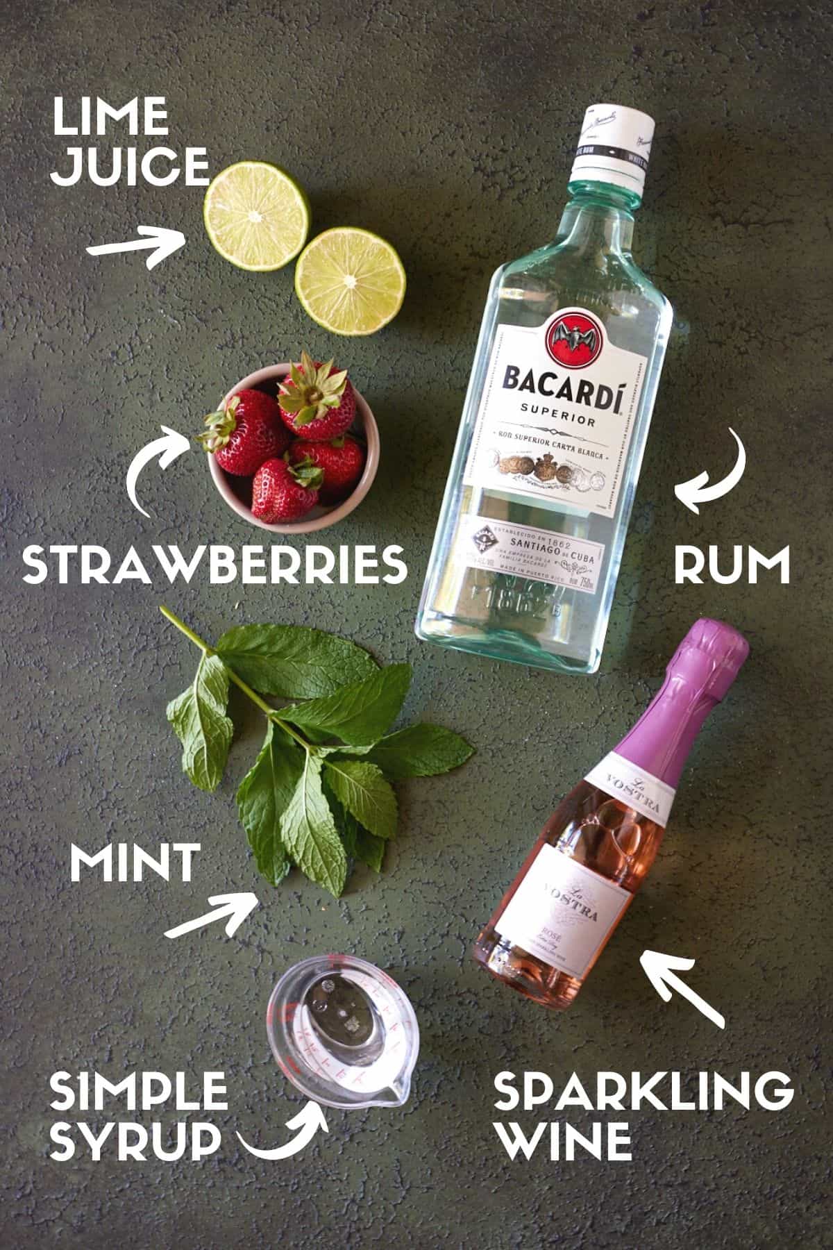 Ingredients for strawberry mojitos, including strawberries, mint, limes, rum and sparkling rosé wine. 