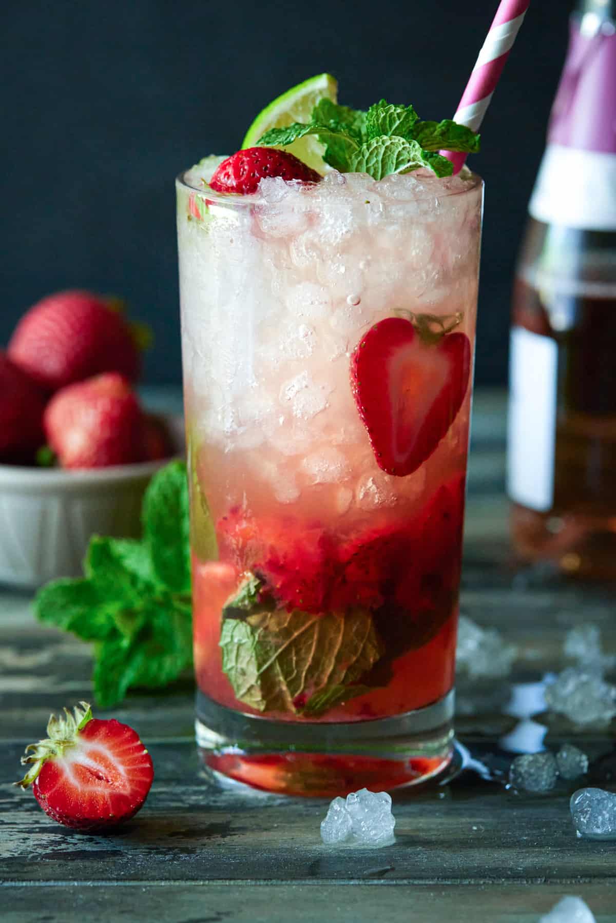 Highball glass filled with Strawberry Mojito. Garnished with limes, strawberries and mint leaves. 