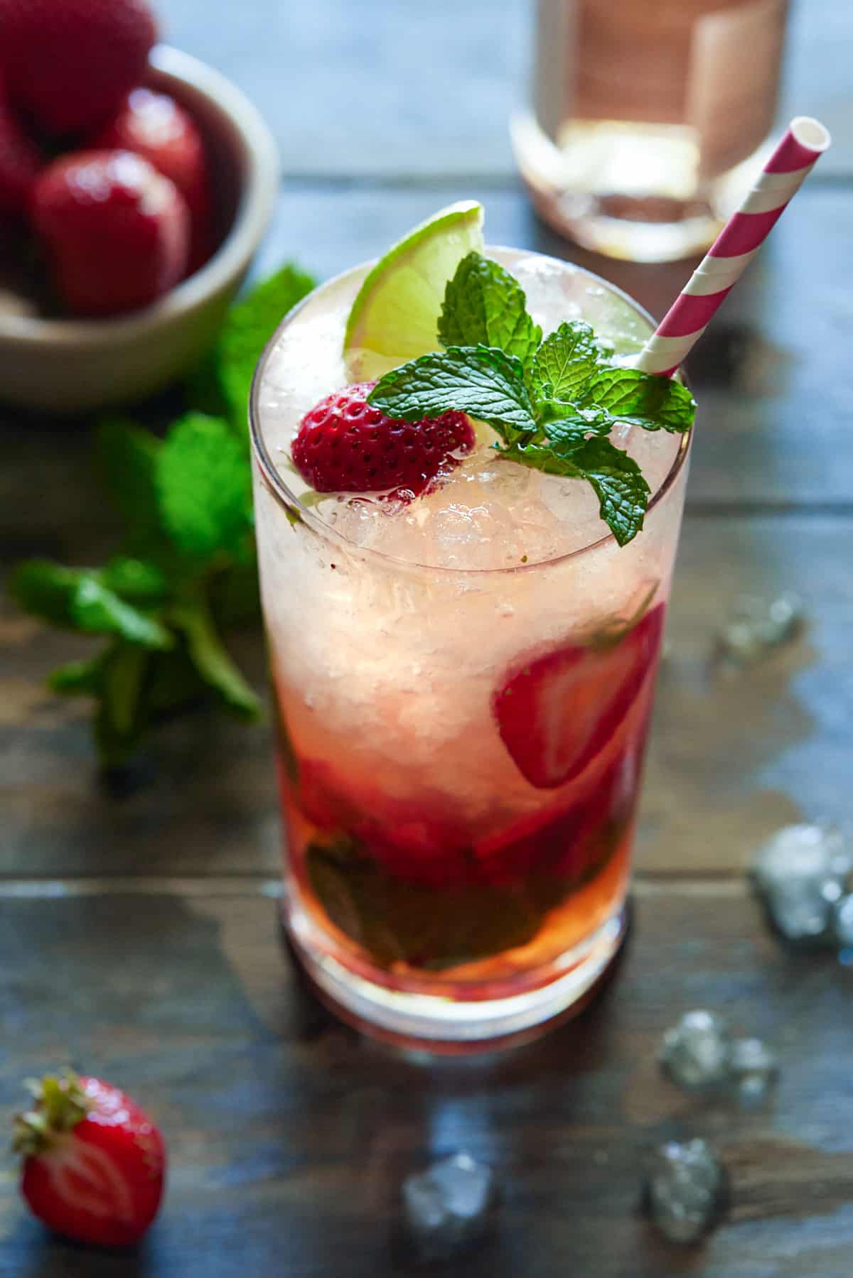 Strawberry Mojito in a highball glass garnished with berries, mint and a pink and white striped straw.