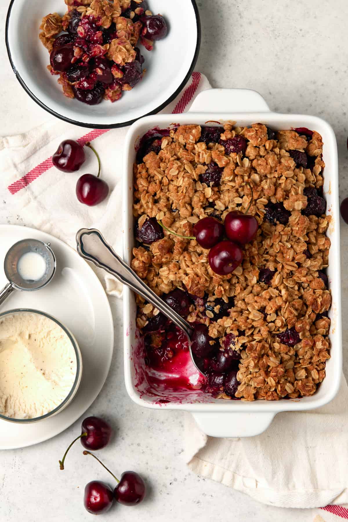 Cherry crisp in a white casserole dish with a serving removed. 