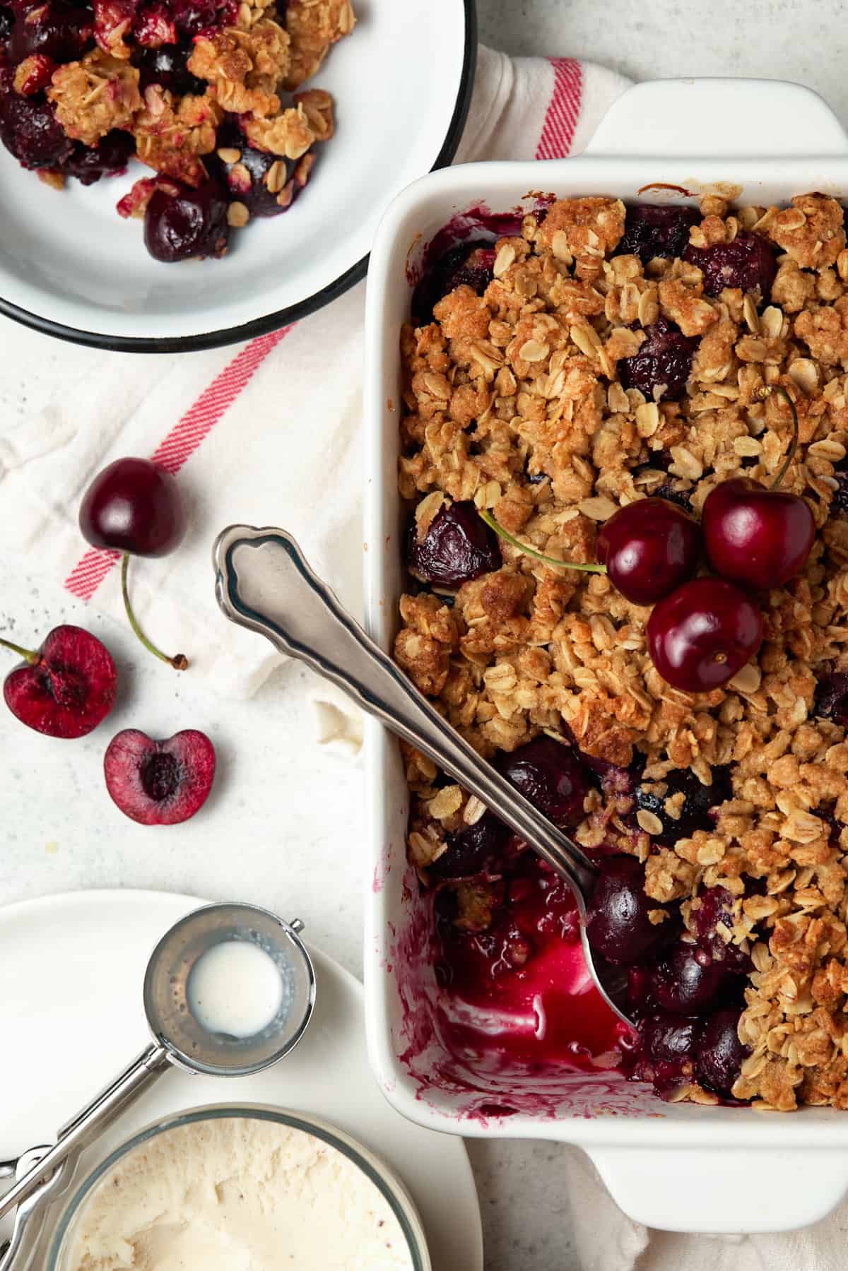 Bowl of cherry crisp by a casserole dish of cherry crisp with a serving removed. 