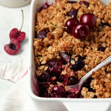 Cherry crisp in a white pan with cherries on top.