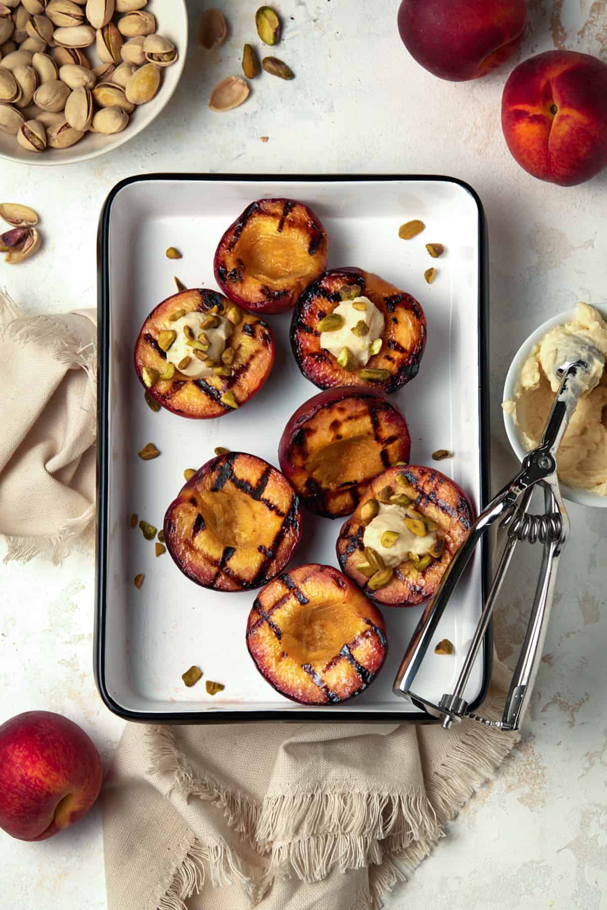 Grilled peach halves in a white enamel tray. Garnished with pistachios and mascarpone cheese. 