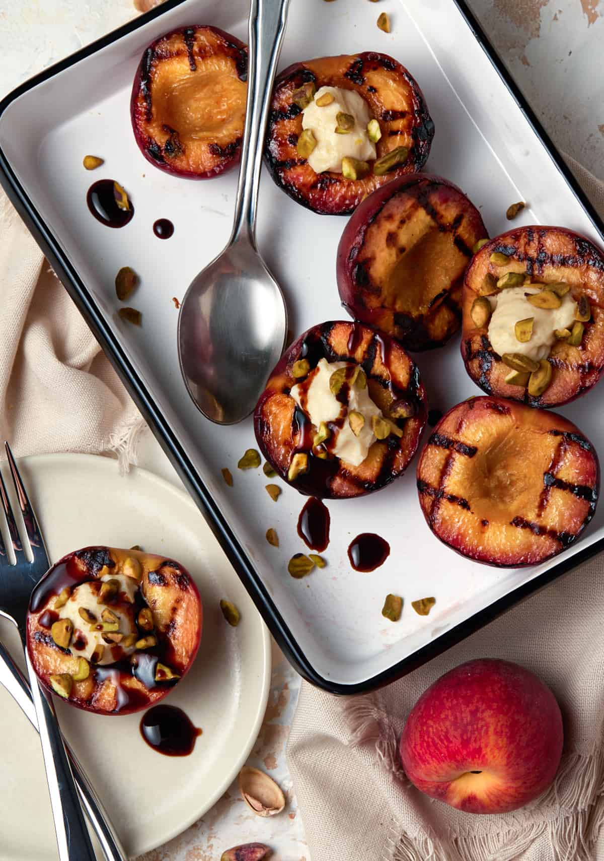 Grilled peach halves on a white tray with balsamic drizzle and pistachios. 
