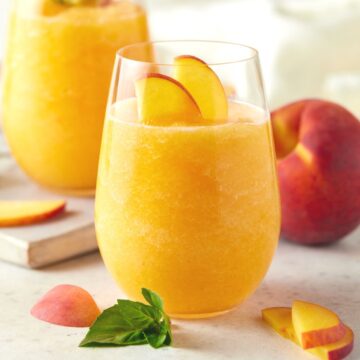 Two glasses of peach wine slushies garnished with fresh peach slices.