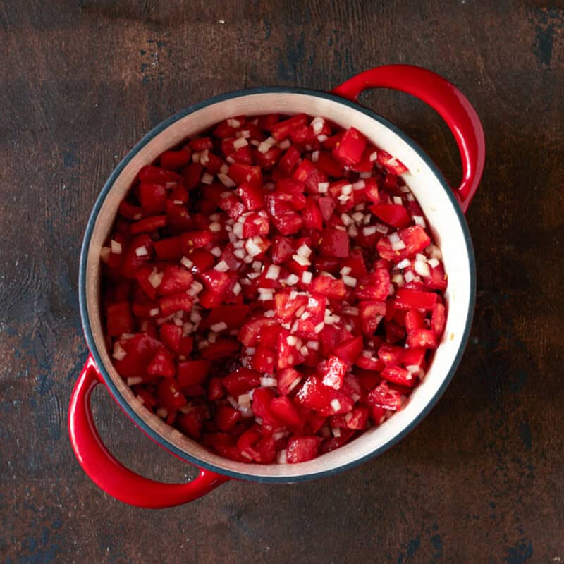 Tomato jam ingredients stirred together in a red dutch oven.