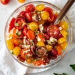 Glass bowl filled with cherry tomato salad with a wooden spoon.