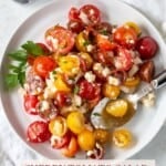White plate filled with cherry tomato salad with feta cheese.