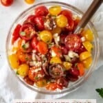 Glass bowl filled with cherry tomato salad with a wooden handle spoon.