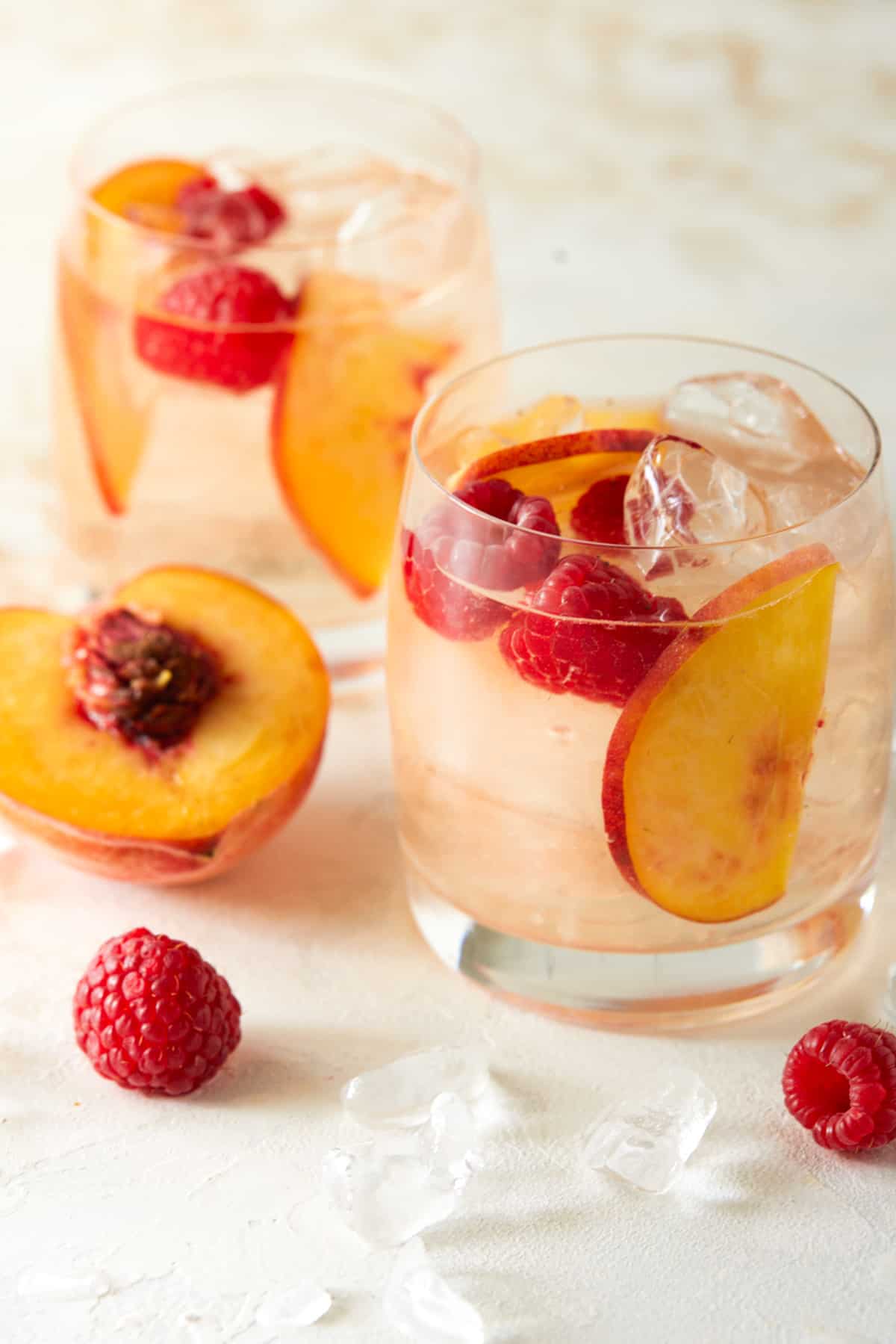 Two glasses of rosé sangria garnished with peach slices and raspberries. 