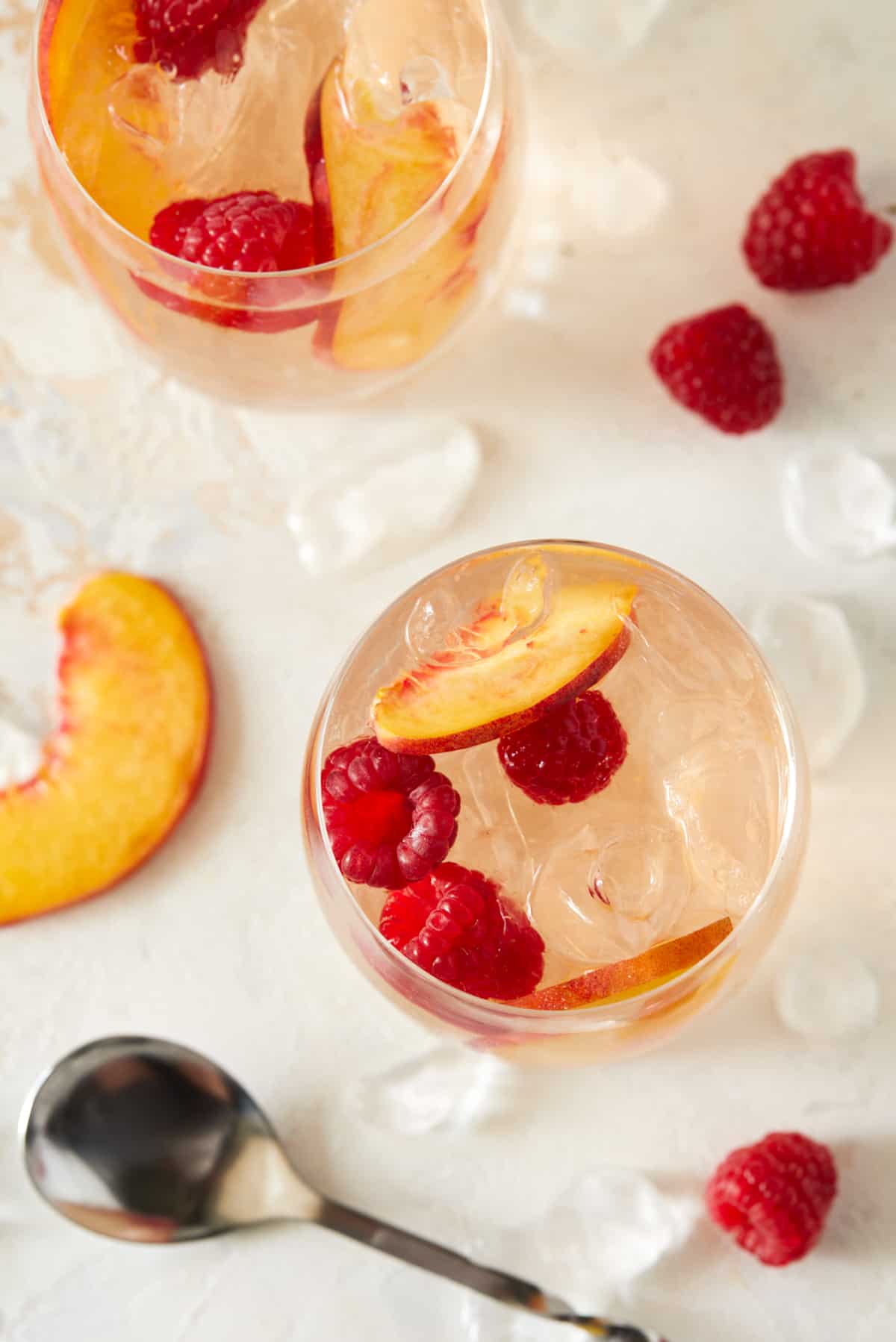 Top down shot of two glasses of rosé sangria with peach slices and raspberries. 
