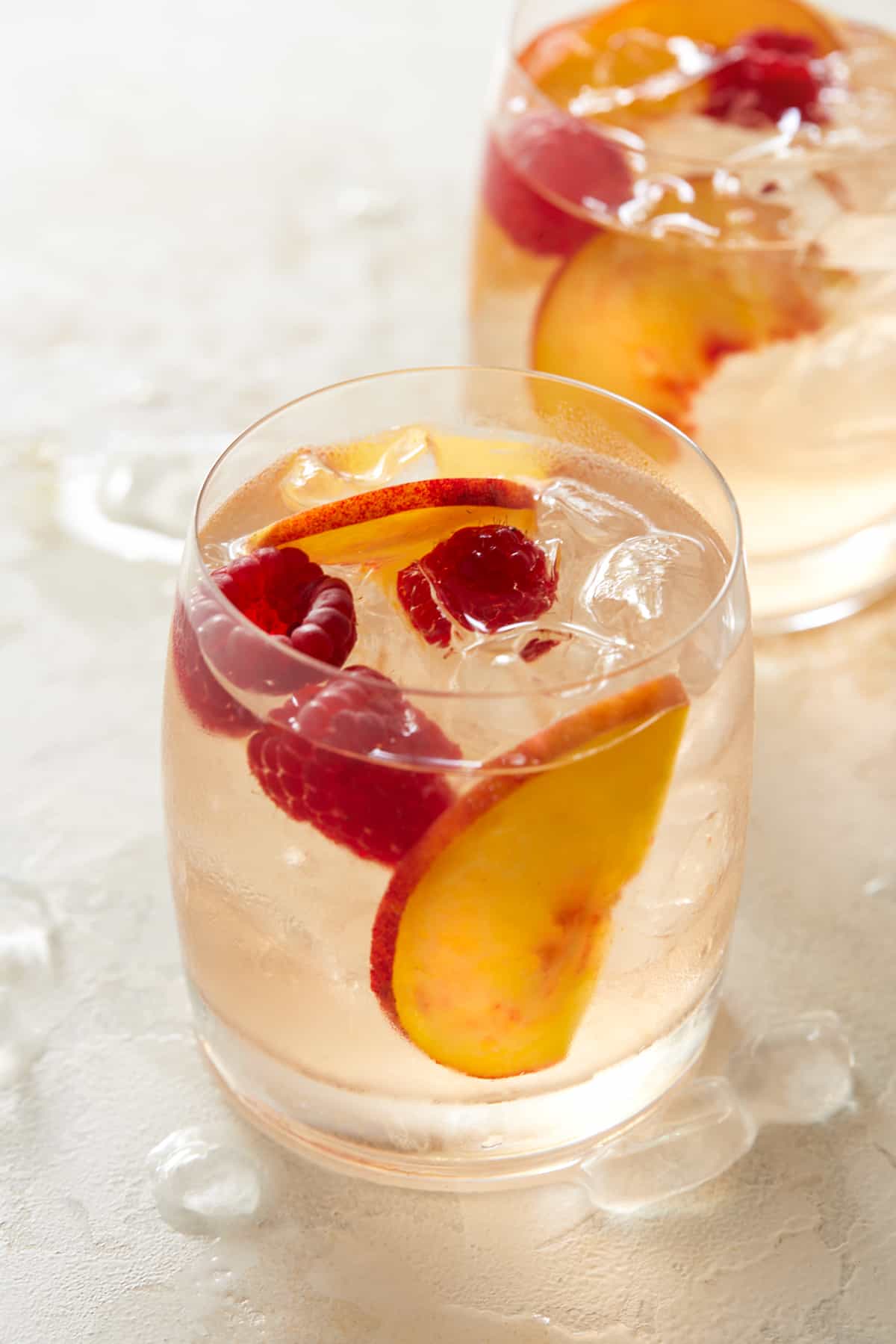 Two glasses of rosé sangria with ice, peach slices and raspberries. 
